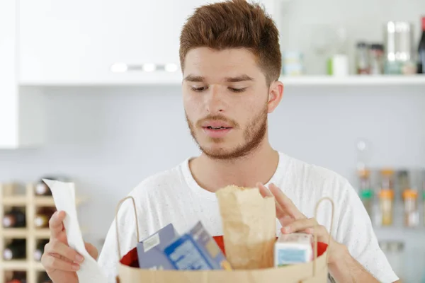 Junger Mann überprüft seine Einkäufe gegen eine Liste — Stockfoto