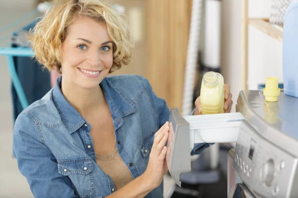 Mulher colocando detergente líquido na máquina de lavar roupa — Fotografia de Stock