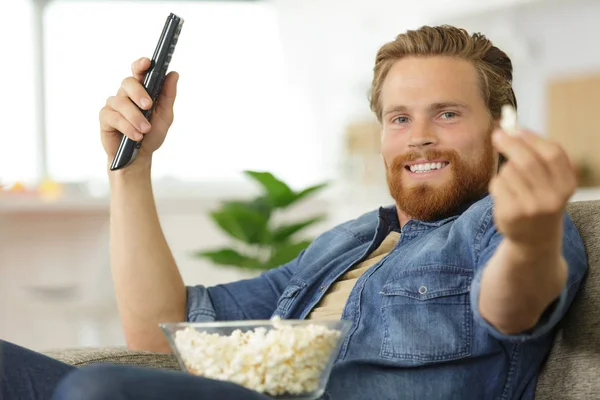 Férfi a kanapén mutatja popcorn ő snack — Stock Fotó