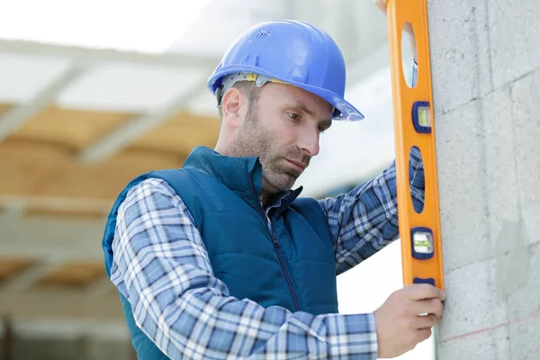 Professional worker in helmet is measuring wall with level — Stock Photo, Image