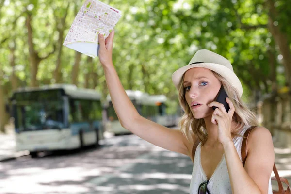 Mujer joven con mapa de la ciudad llamando a un autobús —  Fotos de Stock