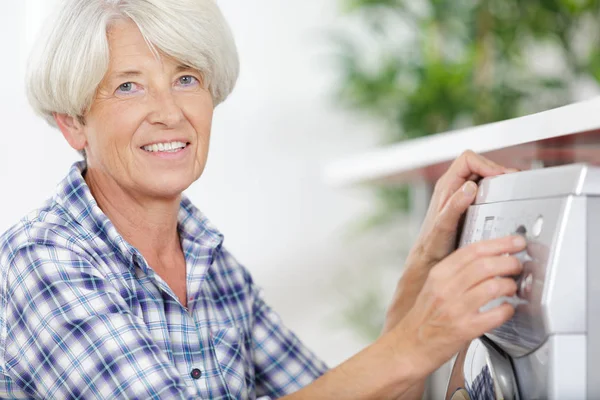 Donna anziana con accanto una lavatrice — Foto Stock