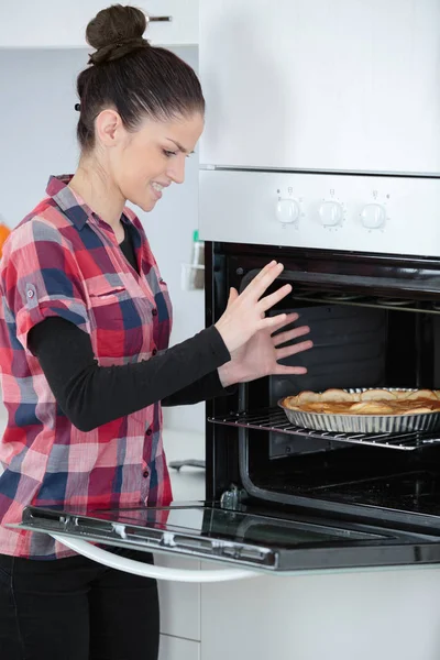 Mujer joven sacando tarta cocida del horno —  Fotos de Stock