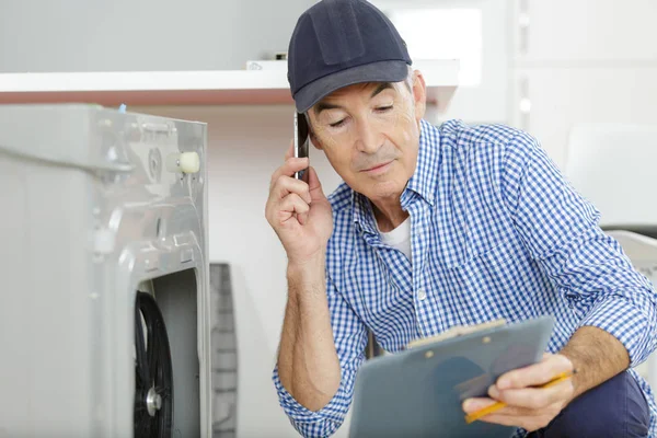 Senior tekniker på telefon med urklipp nära tvättmaskin — Stockfoto