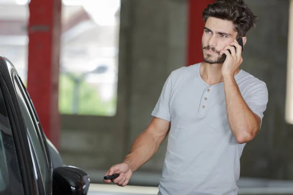 Jonge man aan de telefoon naast de auto — Stockfoto