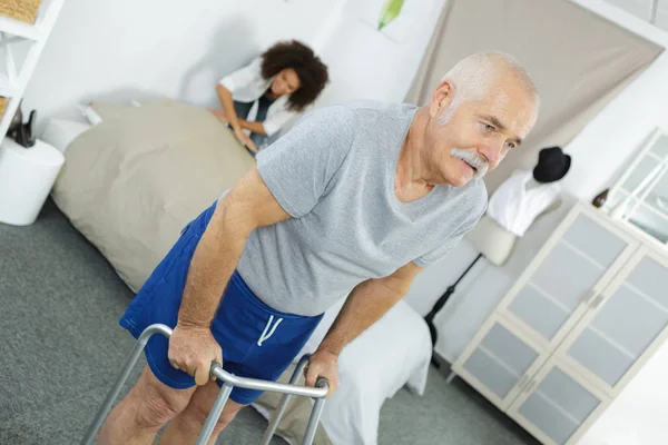 Verpleegkundige helpen een oudere man met een wandelende frame — Stockfoto