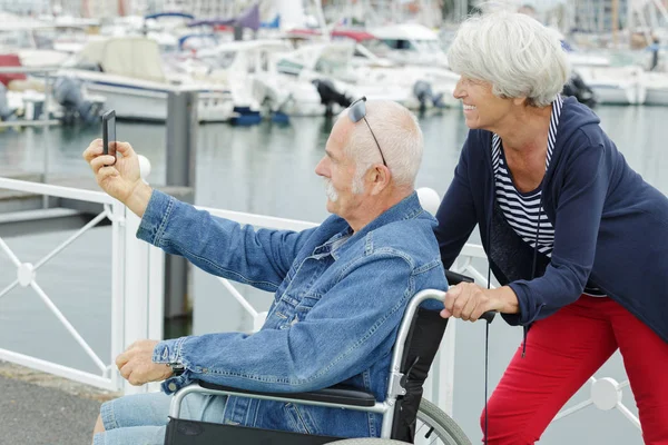 Moglie e suo marito in sedia a rotelle all'aperto facendo un selfie — Foto Stock