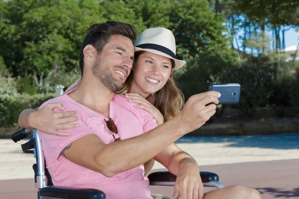 Pareja tomando selfie al aire libre hombre en silla de ruedas —  Fotos de Stock
