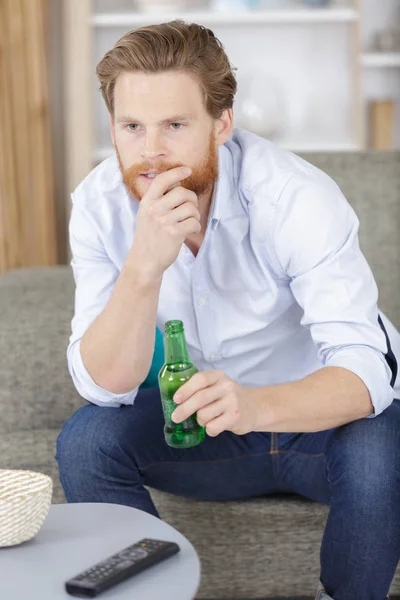 Elinde bira şişesi olan bir adam televizyon izliyor. — Stok fotoğraf
