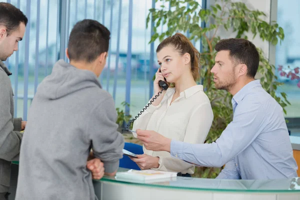 Receptionist pratar i telefon medan gästen väntar — Stockfoto