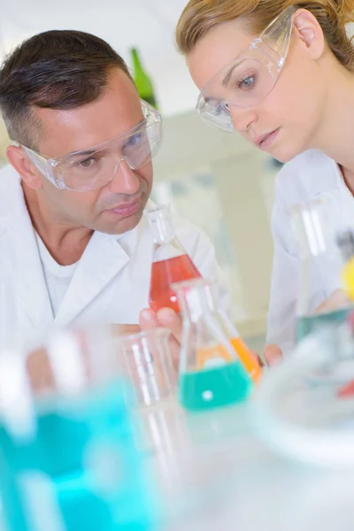 Técnicos de laboratório masculinos e femininos olhando para frascos de vidro — Fotografia de Stock