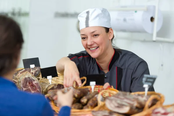 Mulher positiva vendedor segurando bandeja com vários salame — Fotografia de Stock