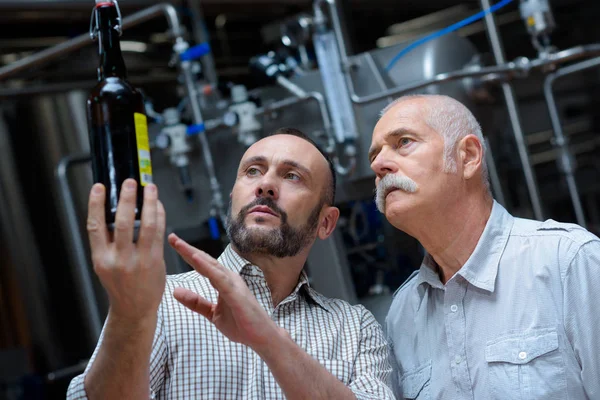 Macho adulto sosteniendo una botella de vino recién producida en la bodega — Foto de Stock