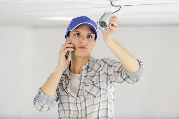 Female technician on the phone fitting cctv camera — Stock Photo, Image