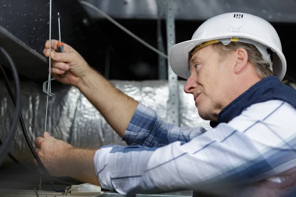 Працівник перевіряє металеву кабельну краватку в просторі даху — стокове фото