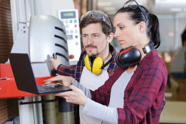 Vrouwelijke timmerman stagiair met behulp van pc in de winkel — Stockfoto