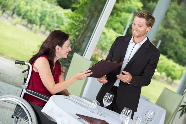 Mulher sorridente em uma cadeira de rodas encomendando em um restaurante — Fotografia de Stock