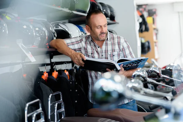 Uomo guardando un catalogo in un negozio di moto — Foto Stock