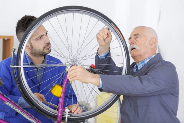 Mecánico de bicicletas y aprendiz de reparación de una bicicleta en el taller —  Fotos de Stock