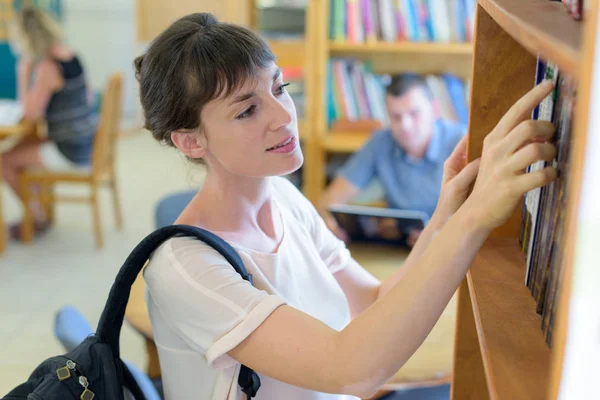 Junge Frau wählt Buch aus Bücherregal — Stockfoto