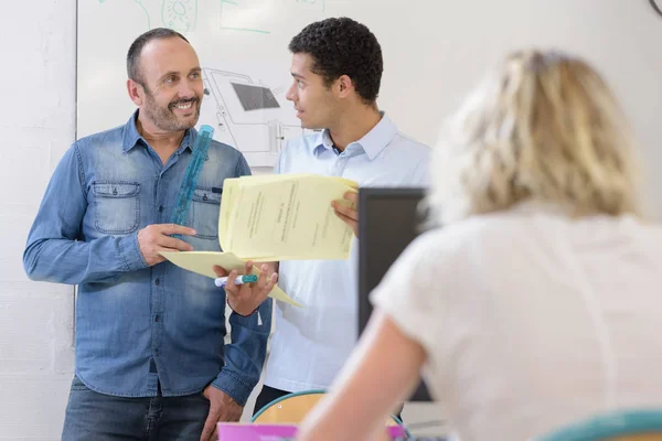 Architect with apprentice looking at papers in office — ストック写真