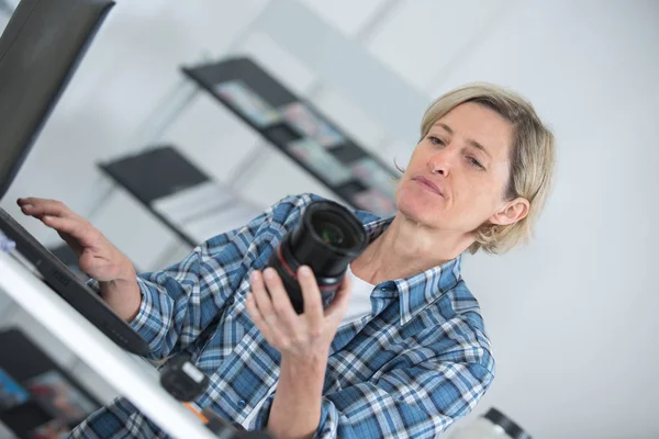 Woman holding camera lens and using laptop — Stock Photo, Image