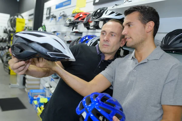 Hombre elige casco para el ciclismo antes de comprar en la tienda de deportes — Foto de Stock