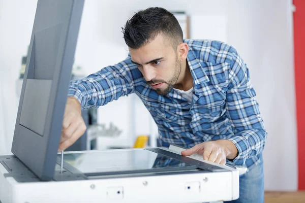 Jovem técnico do sexo masculino reparando máquina fotocopiadora digital — Fotografia de Stock