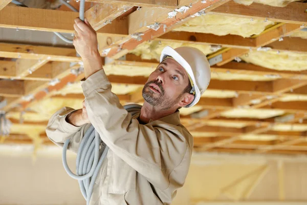 İnşaatçı ahşap tavan kirişlerinden kablo geçiriyor — Stok fotoğraf
