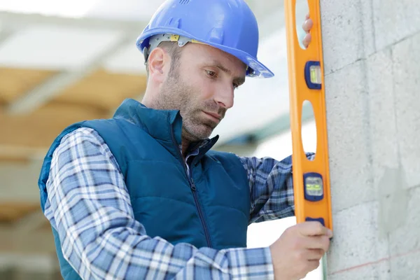 Constructor sostiene una herramienta profesional mientras mide la pared — Foto de Stock