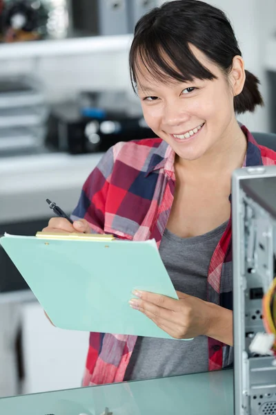 Glückliche Frau sitzt am PC und schreibt auf Papier — Stockfoto