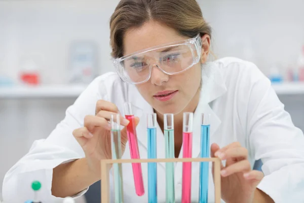 Jonge vrouw die in een erlenmeyer met gekleurde oplossing kijkt — Stockfoto