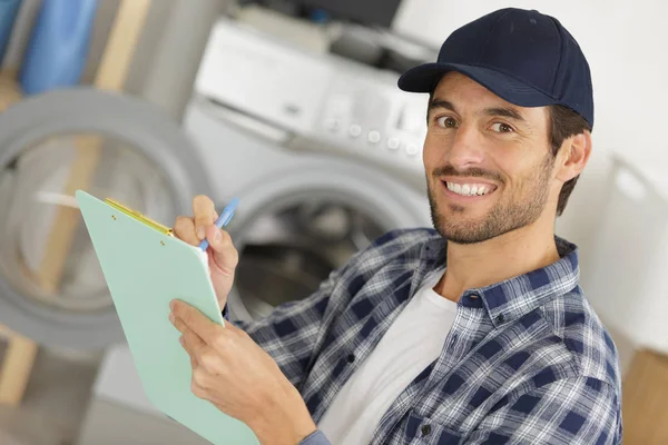 Working man plumber repairs a washing machine in laundry — Stock Photo, Image