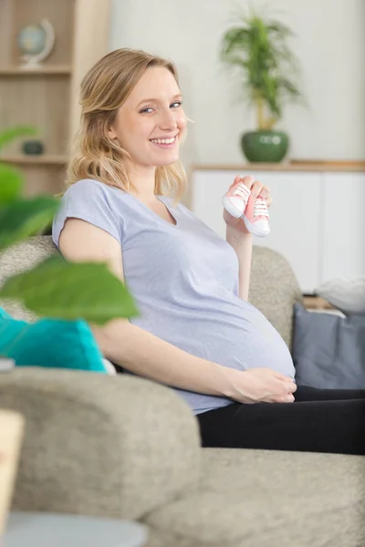 Pregnant woman on sofa holding pink shoes — Stock Photo, Image