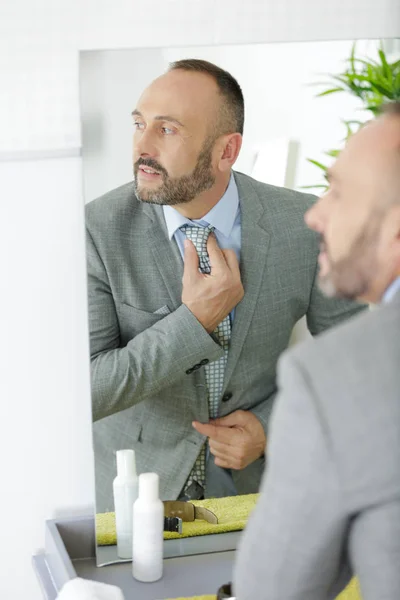 Усміхнений чоловік закріплює краватку на фоні дзеркала — стокове фото