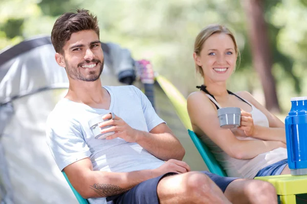 Casal tomando uma bebida de garrafa térmica por sua tenda — Fotografia de Stock