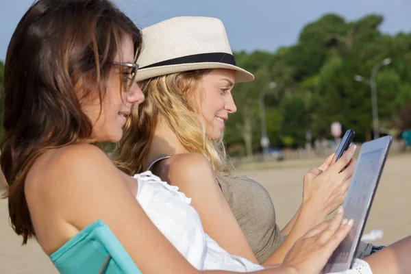 Women using digital gadgets while on the beach — 스톡 사진