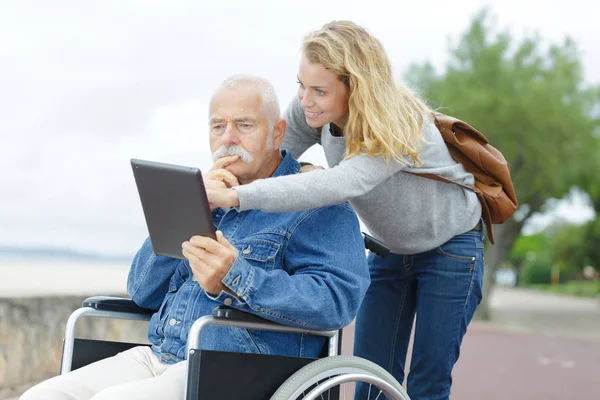 Fille avec son père handicapé en fauteuil roulant en utilisant une tablette — Photo