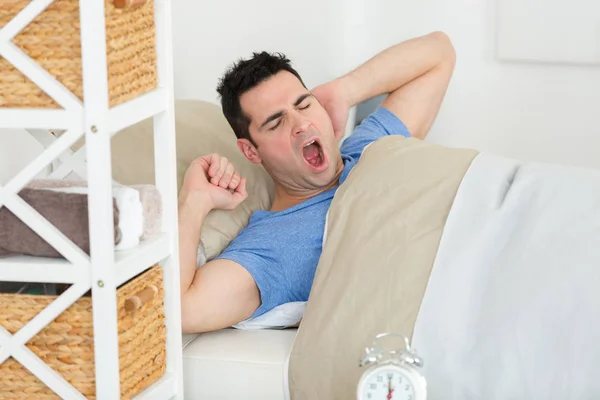 Hombre en la cama bostezando y estirándose mientras despierta — Foto de Stock