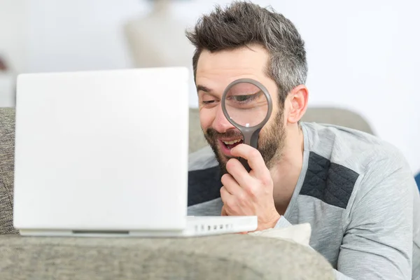 Glad man tittar genom ett förstoringsglas på sin bärbara dator — Stockfoto