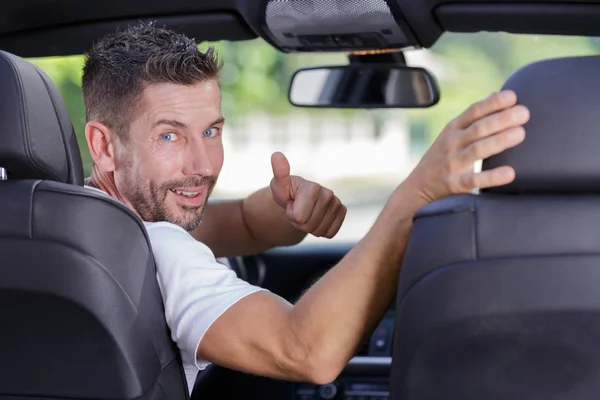 Male driver turning to back of car with thumbs up — Stock Photo, Image