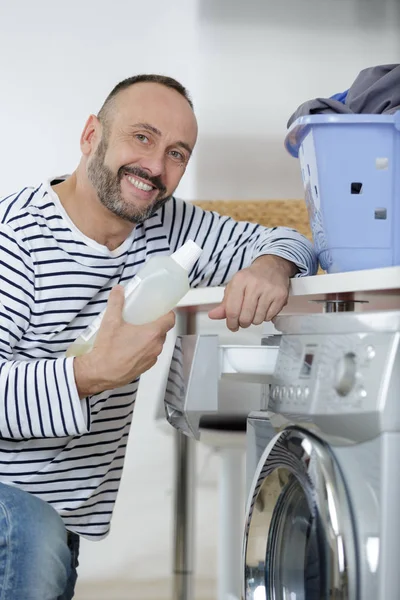 Neşeli adam kirli çamaşırlarını çamaşır makinesine koyuyor. — Stok fotoğraf