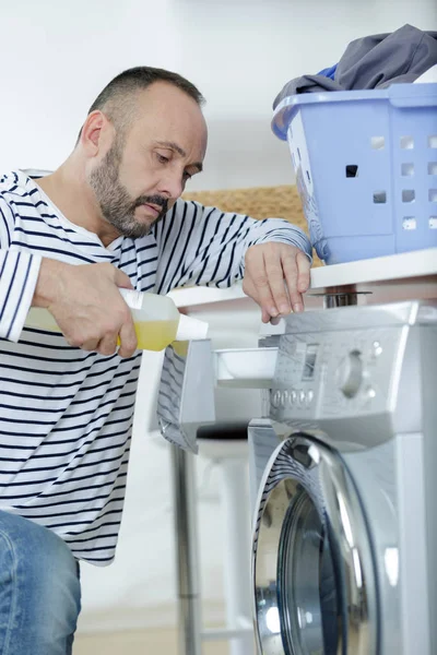 Hombre haciendo lavandería alcanzando el interior de la lavadora —  Fotos de Stock