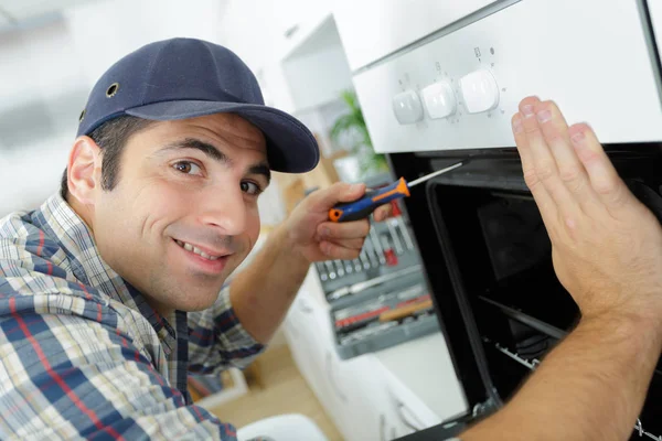 Handyman profissional em macacão reparar forno doméstico na cozinha — Fotografia de Stock