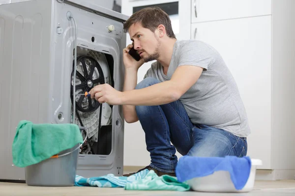 Homme appelant un plombier pour réparer une machine à laver domestique — Photo