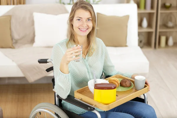 Joven mujer discapacitada en silla de ruedas en casa desayunando —  Fotos de Stock