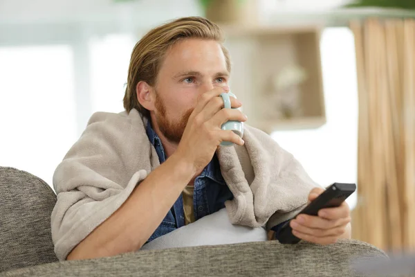 Jonge man kijken Tv in bed en drinken thee — Stockfoto