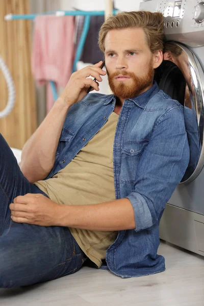 Jonge man man aan de telefoon doen wasserij thuis — Stockfoto