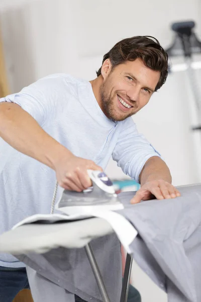 Щасливий чоловік прасує сорочку на залізній дошці вдома — стокове фото