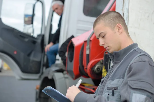 A férfi írótáblára ír, miközben a kamionsofőr várakozik. — Stock Fotó